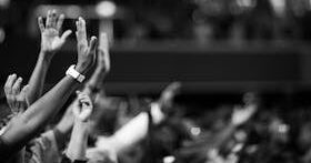 Black and white image of audience with hands raised, capturing concert energy.